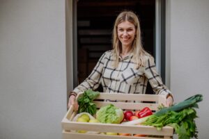 Woman holding delivered crate with vegetales and fruit from local farmer, sustainable lifestyle